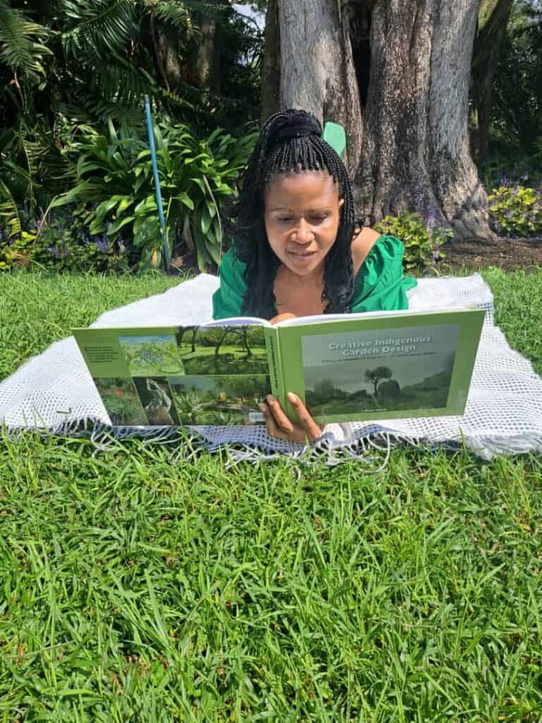 Lush garden landscape with woman reading a gardening book outdoors, promoting sustainable green space design.